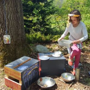 girl plays with toy kitchen in woods