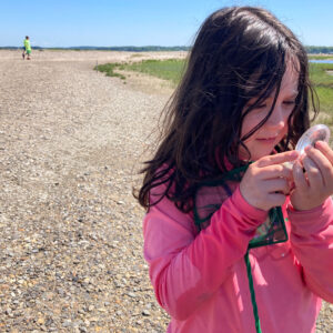 girl examines shell with hand lens