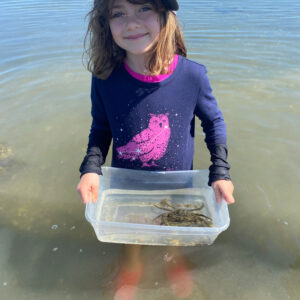 child smiles holding crab in bucket
