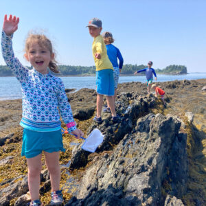 children wave while climbing on rock at beach