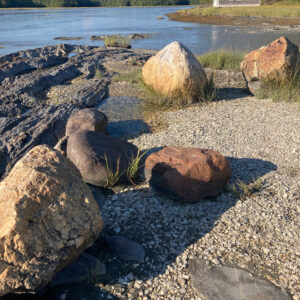 boulders along tide line with boathouse in background
