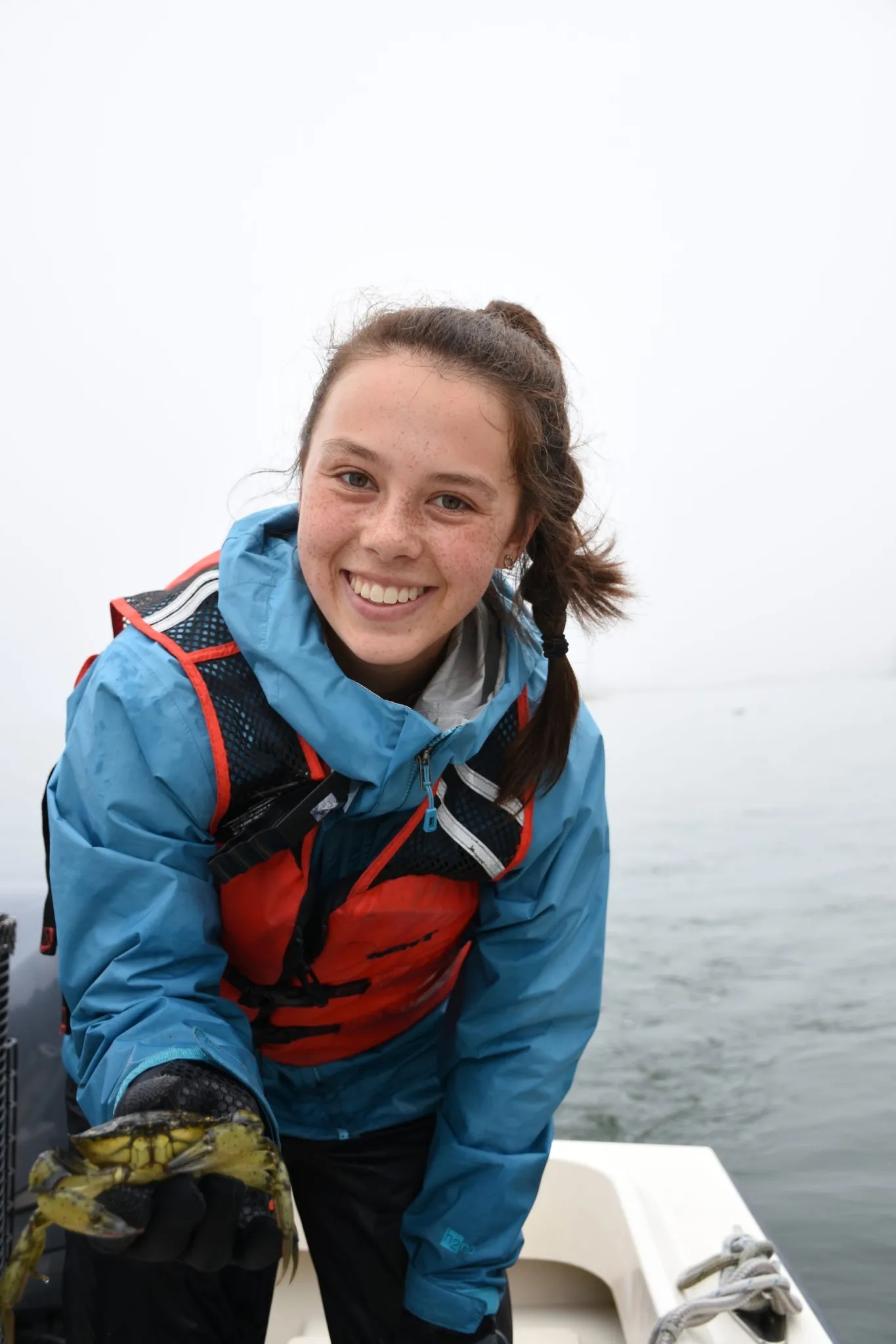 young woman smiles while holding up fist-sized crab for camera