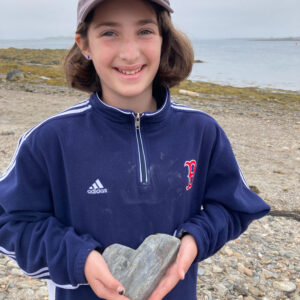 girl in blue jacket smiles holding out heart shaped rock
