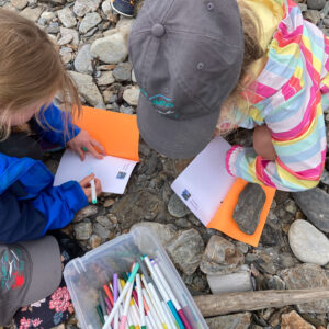 camera looks down at two children drawing in nature journals