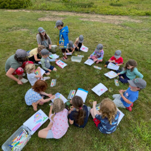 children sit in circle in grass, photo from above