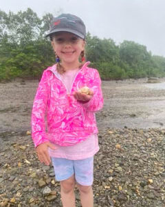 little girl in pink coat smiles holding shell up for camera