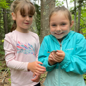 two little girls smile at camera, one with baby snake in hands