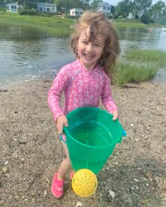 little girl smiles holding green bucket on beach