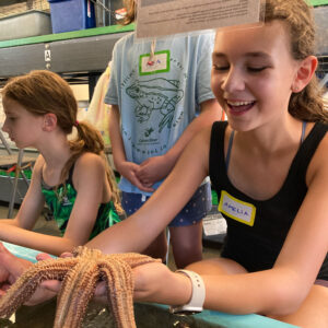 girl smiles while holding large sea star in marine facility