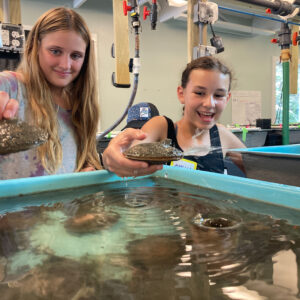 two girls smile holding shellfish over large tank