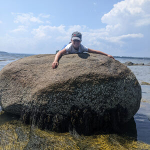 child lays atop large boulder at beach
