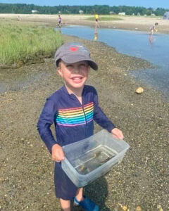 boy smiles holding up bin with marine animals inside