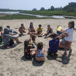 children sit in circle on beach listening to instructor