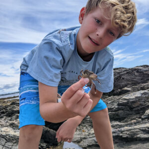 boy crouches in front of camera and holds up small crab