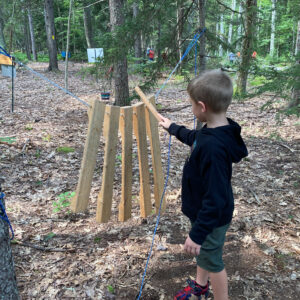 child plays with large wooden hanging xylophone in woods