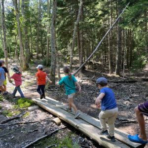 children walk across bog bridge in woods
