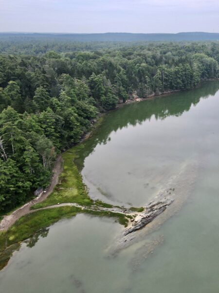 drone view of spit of land that sticks out from forest into calm water