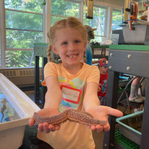 girl smiles and holds sea star up to camera