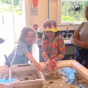 girls smile holding hermit crab over touch tank