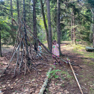 child stands in front of stick hut