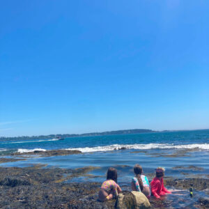 children sit on rock at edge of ocean