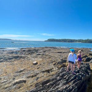 two girls stand on rock overlooking ocean
