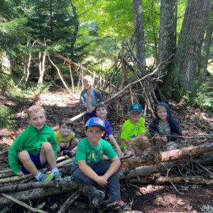 children sitting on fallen tree smile at camera