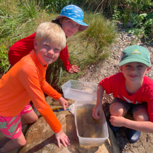 three boys smile around collection bucket