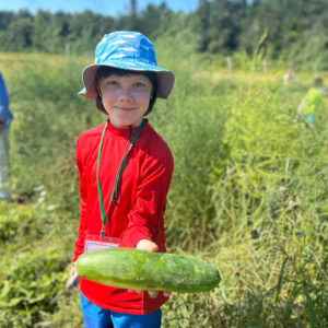smiling boy holds up harvested cucumber at community garden