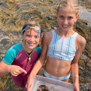 two girls smile for camera holding baby lobster