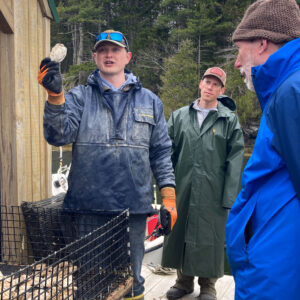 man holds up oyster while talking to group of onlookers