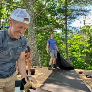 man smiles as others re-roof a shed