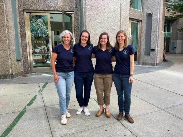 four women smile for camera in matching blue shirts