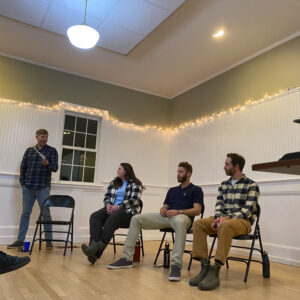 one person stands and three sit in chairs while talking